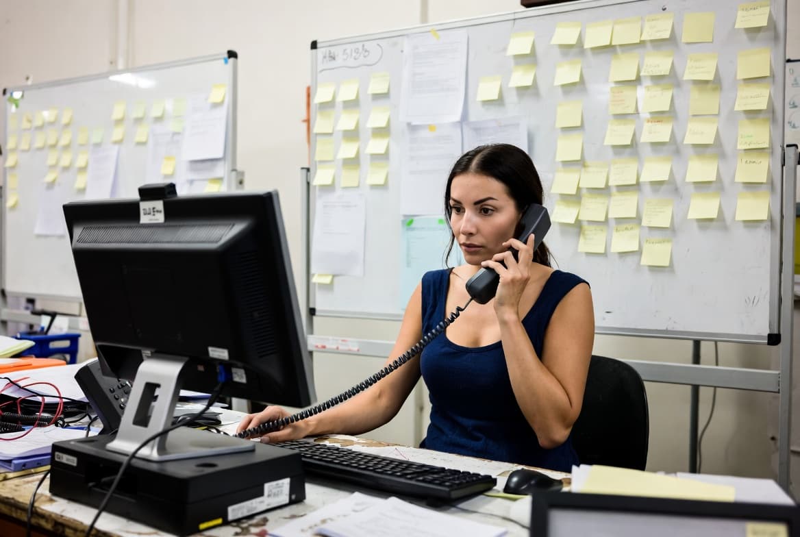 A busy dispatch office with whiteboards, sticky notes, and a phone ringing — the kind of Tuesday morning every owner knows.